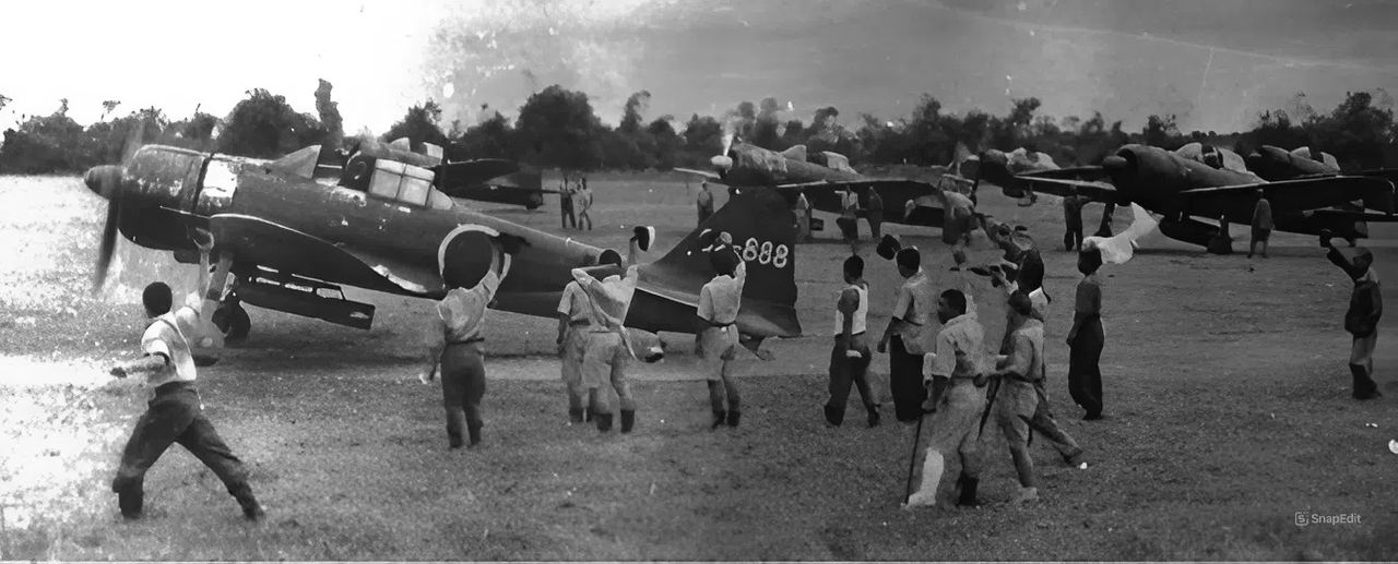 Những chiếc Zero-sen A6M3 mệt mỏi vì chiến tranh, mang theo bom 551lb, được hộ tống bởi các A6M5 trang bị thùng dầu phụ, lăn bánh ra đường băng tại Davao, trên đảo Mindanao, vào ngày 25 tháng 10 năm 1944 để báo hiệu sự khởi đầu của chiến dịch kamikaze. Sau nhiều lần xuất kích bị hủy bỏ trong những ngày trước đó, khi không tìm thấy mục tiêu nào, các cuộc tấn công kamikaze thành công đầu tiên đã diễn ra vào ngày này khi các tàu sân bay hộ tống của “Taffy 1” và “Taffy 3” bị đánh trúng nặng nề. (via Henry Sakaida)