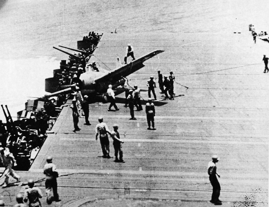 Một chiếc Grumman F4F-4 Wildcat (số hiệu BuNo 5246) thuộc Phi đội Chiến đấu 72 (VF-72) từ tàu sân bay USS Hornet (CV-8) trượt trên boong sau khi hạ cánh xuống tàu USS Enterprise (CV-6) khi tàu sân bay này thực hiện các thao tác né tránh dữ dội dưới sự tấn công của máy bay Nhật. Các thủy thủ đang dùng dây kéo chiếc máy bay trên đường băng xuống, kéo nó ra khỏi vị trí nguy hiểm gần khu vực đặt súng. Công việc cứu hộ vẫn tiếp tục bất chấp nguy cơ bị không kích lần nữa của quân Nhật. Các pháo thủ không chú ý đến sự hỗn loạn trên đầu, họ dán mắt lên bầu trời để tìm kiếm dấu hiệu của máy bay địch. (NHHC)