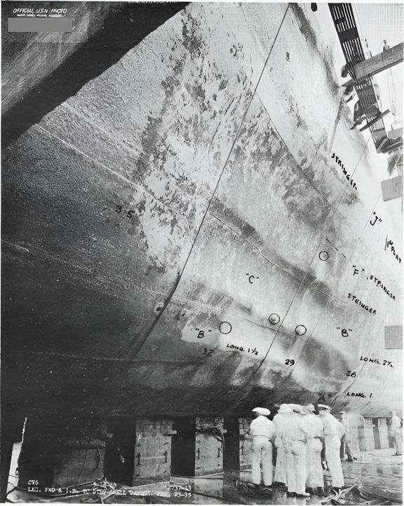 Vị trí của quả bom nổ sượt thứ hai bên mạn tàu. Quang cảnh thiệt hại đối với vỏ tàu, với các vết nứt nhỏ trên tấm vỏ được khoanh tròn. (NHHC)