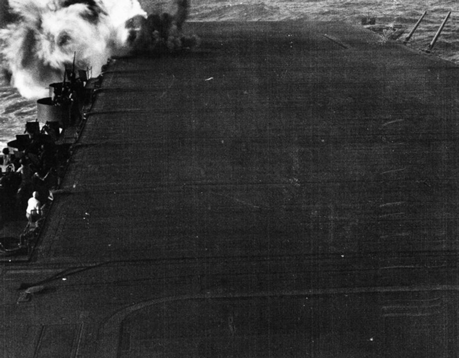 Một quả bom đánh trúng vào bệ pháo 5 inch phía sau mạn phải của tàu Enterprise , phá hủy nó và giết chết gần như toàn bộ 45 thành viên phi hành đoàn. Đây là quả bom thứ hai đánh trúng tàu Enterprise trong cuộc tấn công. Bên cạnh gần thang nâng có lỗ đang bốc khói do quả bom thứ nhất gây ra. (NHHC)