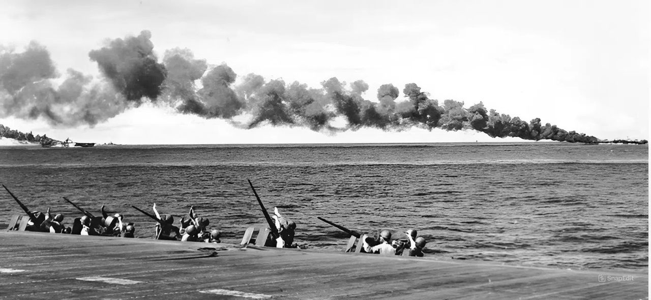 Các thành viên của Đội Thủy quân lục chiến trên tàu Enterprise che mắt khỏi ánh mặt trời khi họ quét bầu trời tìm máy bay kamikaze vào ngày 30 tháng 10 năm 1944. Các tàu sân bay trong cùng lực lượng TG 38.4, USS Franklin (CV-13) (bên trái) và USS Belleau Wood (CVL-24), đang bốc cháy dữ dội phía sau họ, sau khi đã bị các máy bay cảm tử đánh trúng. Franklin bị loại khỏi vòng chiến cho đến tháng 3 năm 1945 và chịu tổn thất 56 người chết cùng 60 người bị thương, trong khi Belleau Wood ghi nhận 92 người chết và 97 người bị thương. Tàu sân bay hạng nhẹ này không trở lại hoạt động cho đến tháng 2 năm 1945. (NARA)