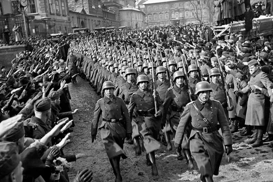 <i>Quân Đức diễu binh qua thủ đô Praha của Tiệp Khắc, trong khi những người Slovak ủng hộ Đức giơ tay chào theo kiểu Hitler, năm 1939. Slovakia là "đồng minh chiến đấu" của Đức dưới chế độ Slovak cộng tác với phát xít.</i>