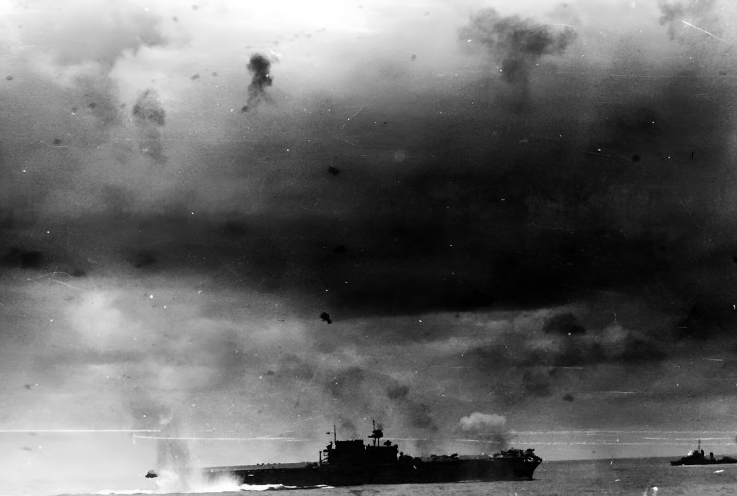 Một quả bom được thả từ máy bay ném bom bổ nhào Type 99 phát nổ bên mạn phải của tàu sân bay Enterprise. Bức ảnh được chụp từ tàu tuần dương hạng nặng USS Portland (CA-33). Chú ý tàu khu trục lớp Mahan ở bên phải. (NHHC)