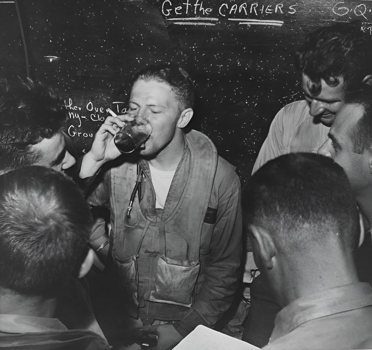 Một phi công của VT-28 trên tàu sân bay hạng nhẹ Monterey thư giãn trong phòng trực ban (ready room) sau khi trở về từ đòn không kích ngày 20 tháng 6. VT-28 đã điều bốn chiếc Avenger tham gia nhiệm vụ và mất một chiếc do nguyên nhân khai thác. Lưu ý dòng chỉ thị trên bảng phấn trong phòng trực ban: “Get the Carriers” (Hãy tiêu diệt các tàu sân bay). (NHHC)