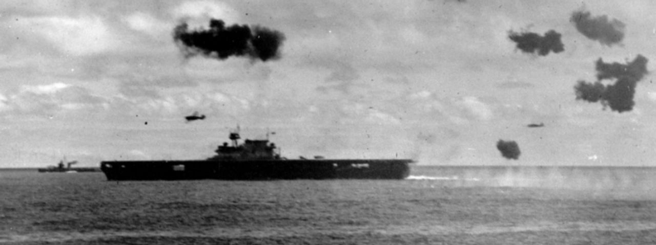 Nhóm thứ hai gồm năm chiếc B5N2 tấn công tàu Yorktown vào ngày 4 tháng 6 đã ghi được hai quả ngư lôi trúng đích. Hai chiếc máy bay trong số đó có thể nhìn thấy ở đây, một chiếc phía trên tàu sân bay và một chiếc ở đuôi tàu, sau khi đã thả ngư lôi. Trong trường hợp này, hỏa lực phòng không mạnh mẽ đã không thể bảo vệ được tàu Yorktown. Bức ảnh được chụp từ tàu tuần dương hạng nặng Pensacola, và tàu khu trục phía trước mũi tàu sân bay có thể là Morris. (NHHC)