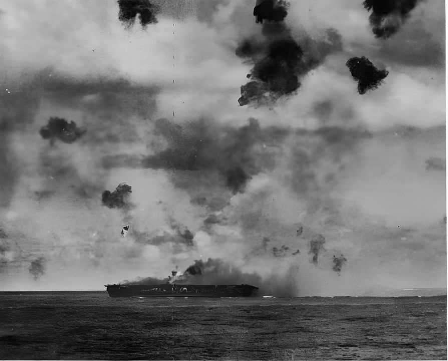 Hornet trong giai đoạn cuối của cuộc tấn công buổi sáng ngay sau khi một máy bay ném bom bổ nhào của địch vòng qua mũi tàu và đâm vào boong hành lang bên mạn trái ngay phía trước thang máy số 1. Chú ý khói dày đặc ở giữa tàu do vụ va chạm của máy bay ném bom bổ nhào đầu tiên của địch. Lưu ý độ nghiêng về mạn phải do trúng hai quả ngư lôi.