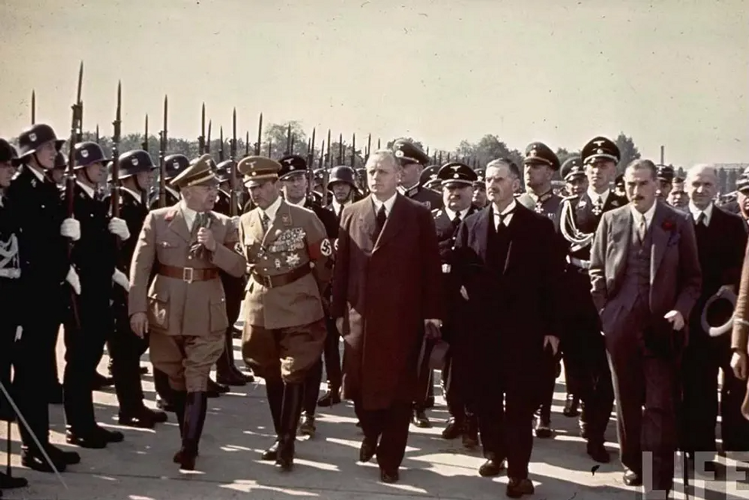 <i>Thủ tướng Anh Neville Chamberlain (hàng đầu, thứ hai từ bên phải) đi ngang qua đội danh dự trong buổi tiếp đón khi ông đến sân bay Oberwiesenfeld trên đường đến cuộc họp với Adolf Hitler, ngày 28/09/1938. Trong ảnh, từ trái sang phải, chính trị gia người Đức Gauleiter Adolf Wagner, SA-Obergruppenführer Franz Ritter von Epp, Ngoại trưởng Đức Joachim von Ribbentrop, Chamberlain và Đại sứ Anh tại Đức Sir Neville Henderson.</i>