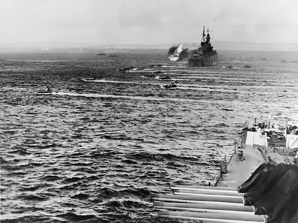 Khung cảnh này cho thấy Ngày D (D-Day) tại Saipan, với các xe lội nước đổ bộ chở Thủy quân lục chiến đang hướng vào bãi biển, di chuyển ngang qua các tàu tuần dương đang tiến hành bắn phá yểm trợ. Con tàu ở phía sau là tàu tuần dương hạng nặng Indianapolis. Mặc dù con tàu này được biết đến nhiều hơn vì bị tàu ngầm Nhật Bản đánh chìm vào tháng 7 năm 1945, gây ra một trong những thảm họa tổn thất sinh mạng kinh hoàng nhất của Hải quân Mỹ, nhưng trong phần lớn thời gian của cuộc chiến, Indianapolis phục vụ với vai trò soái hạm của Hạm đội 5, nơi Đô đốc Spruance trực tiếp chỉ huy. (NHHC)