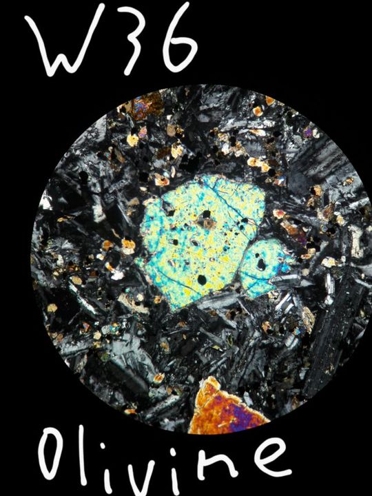 Nhìn từ cực chéo. Các hạt olivin đầy màu sắc mang hình dạng quả bóng đá đặc trưng. Cũng lưu ý rằng màu sắc ở các cạnh có xu hướng hơi khác so với màu sắc ở giữa, và các màu giao thoa sáng. Các hạt dài màu xám óng ánh bao quanh olivin là plagioclase fenspat