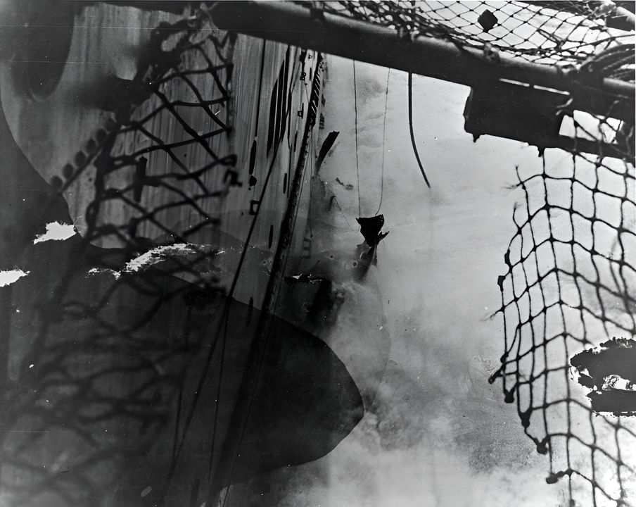 Nhìn từ mạn trái tàu USS Lexington, nhìn từ phía sau và xuống qua lớp lưới cứu sinh bị rách trên sàn đáp, cho thấy thiệt hại từ quả ngư lôi trúng đích sau cùng trong hai quả trong Trận chiến Biển San Hô, ngày 8 tháng 5 năm 1942. Quả ngư lôi trúng đích này nằm ở khoảng Khung 85, và làm nổ tung một số tấm vỏ tàu, như có thể thấy ở mực nước trong bức ảnh này. (NHHC)