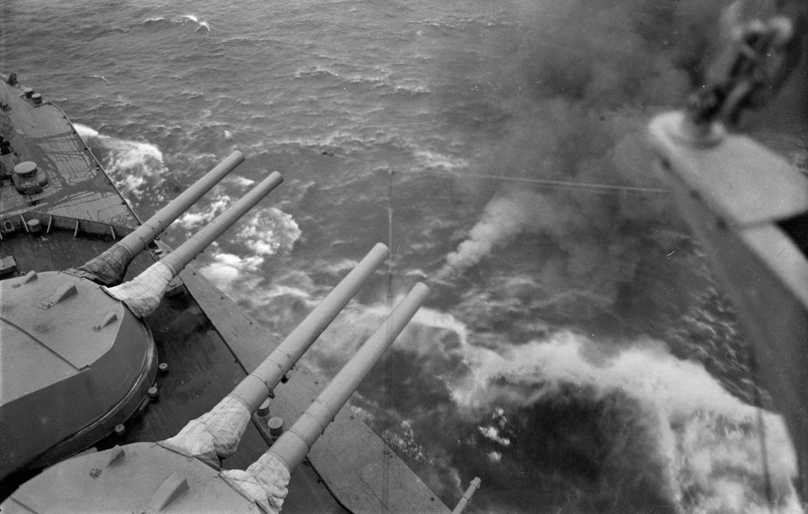 Góc nhìn từ mũi tàu HMS Queen Elizabeth (1913), nhìn xuống mạn phải của sàn mũi tàu. Tháp pháo 'A' và 'B' được xoay ra phía mũi phải để luyện tập bắn. Có thể thấy khói bốc lên từ khẩu pháo 15 inch bên phải của tháp pháo 'B', vốn vừa mới giật lùi sau khi bắn. Nòng pháo 6 inch gắn trên ụ pháo có thể thấy ở phía dưới bức ảnh.