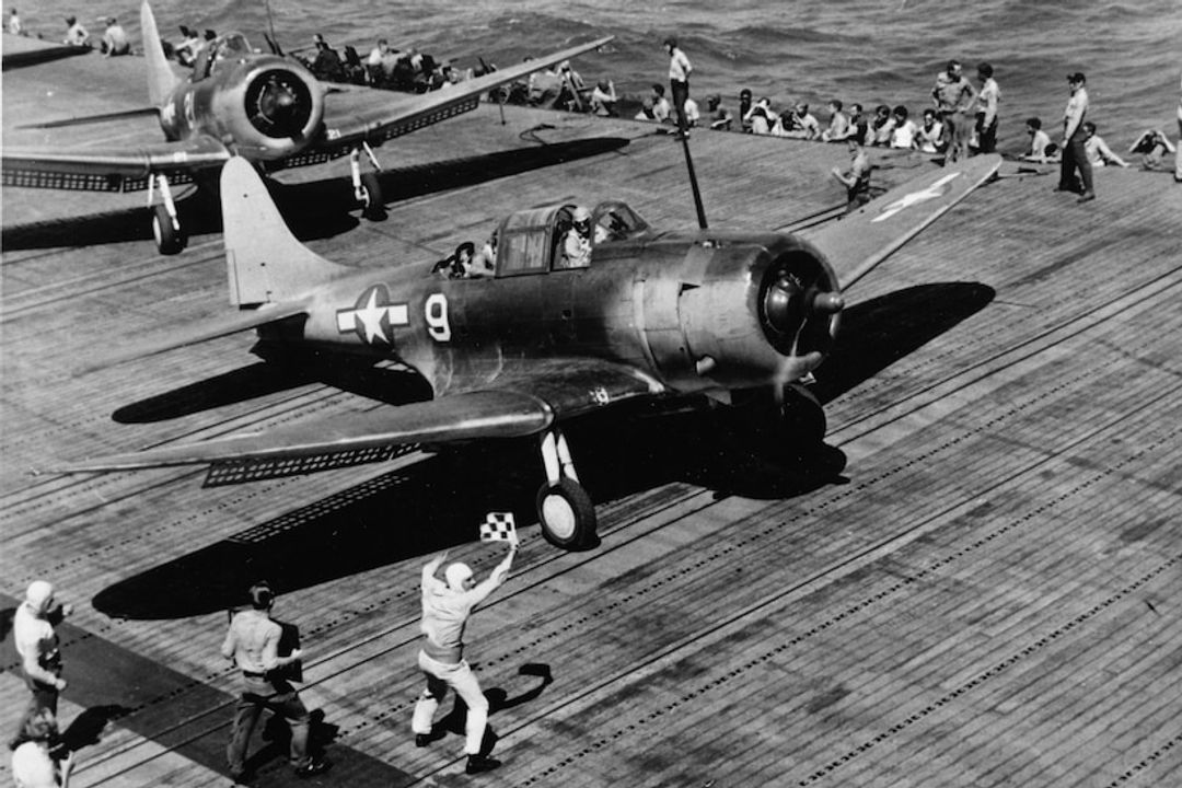 Douglas SBD Dauntless tiếp tục phục vụ trên tàu sân bay cho tới giữa năm 1944, khi cuối cùng bị Helldiver thay thế. Dauntless bền bỉ, dễ điều khiển, và quan trọng nhất là một nền tảng ném bom bổ nhào rất chính xác. Tuy nhiên, nó bị hạn chế về tầm bay và tốc độ. Trong bức ảnh này, sĩ quan điều hành cất cánh đã giương cao lá cờ kẻ ô, sẵn sàng ra hiệu cho phi công SBD thuộc VB-5 bắt đầu lượt tăng tốc cất cánh từ sàn tàu Yorktown. (Naval History and Heritage Command, Photo Archives, Naval Subject Collection)