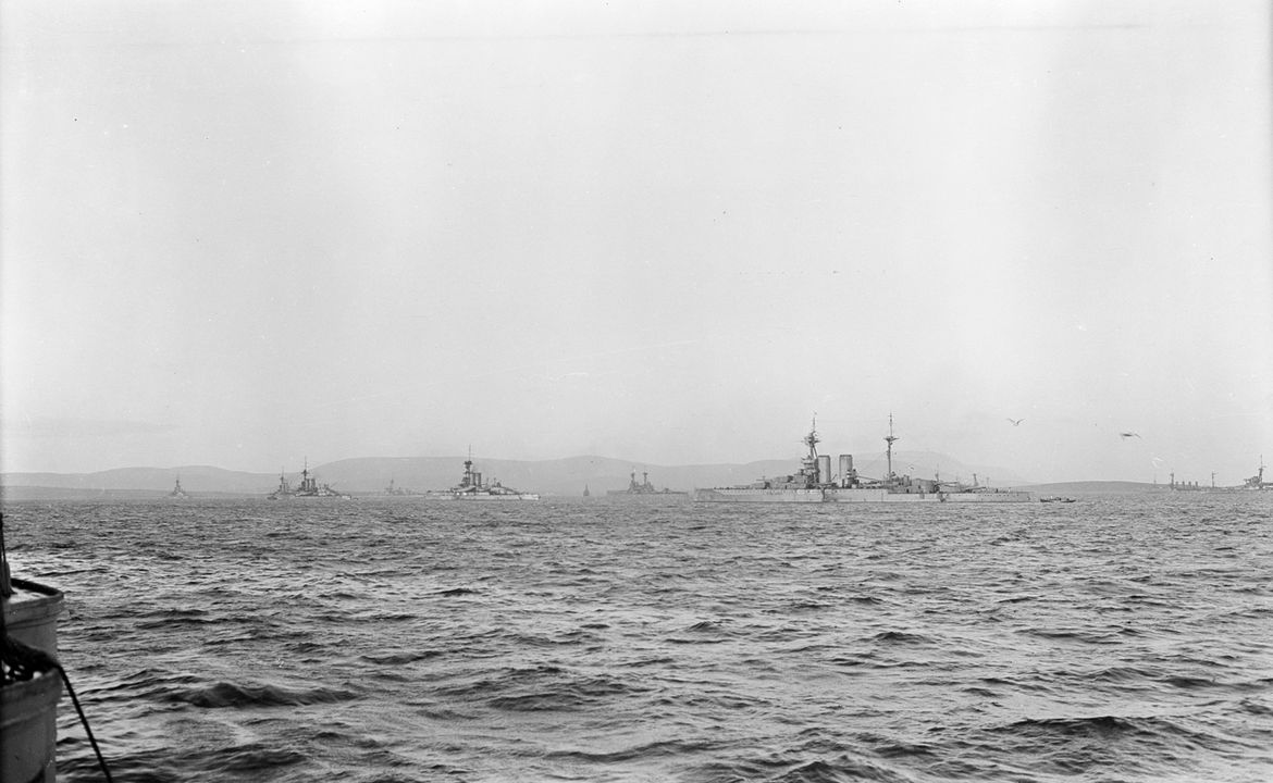 Toàn cảnh các tàu của Đại Hạm đội neo đậu tại Scapa Flow, chụp từ mạn phải sau cuối boong trên của thiết giáp hạm HMS Queen Elizabeth (1913). Các ụ pháo 6 inch sau được bịt kín chỉ nhìn thấy ở phía dưới bên trái của bức ảnh. Thiết giáp hạm gần nhất là tàu chị em và là đồng đội của Queen Elizabeth, HMS Barham (1914). Bốn tàu phía trước Barham là các tàu thuộc Hải đội 1 thuộc Hải đoàn Thiết giáp hạm số 2 bao gồm từ trái sang phải là HMS Erin (1913), HMS King George V (1911), HMS Ajax (1912) và HMS Centurion (1911). Có thể nhìn thấy ở khoảng cách giữa Ajax và Centurion là một thiết giáp hạm thuộc lớp Colossus. Tàu chị em của nó có thể được nhìn thấy ở cực bên phải của bức ảnh (chỉ phần trước) với một tàu tuần dương bọc thép bốn ống khói ở phía xa. Ở trung tâm của bức ảnh ngay phía sau mũi tàu Barham là một thiết giáp hạm thuộc lớp Bellerophon hoặc St Vincent. Sự hiện diện của những con tàu này cho thấy sự hiện diện của cả hai hải đội thuộc Phi đoàn Thiết giáp hạm số 1.