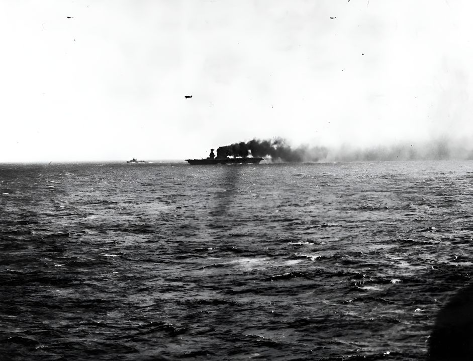 Lexington bốc cháy và chìm ở mũi tàu, nhưng vẫn tiếp tục hoạt động và vận hành máy bay, kể cả khi bị trúng ngư lôi và bom. Bức ảnh này được chụp vào khoảng trưa ngày 8 tháng 5 năm 1942, trước khi đám cháy bị gây ra bởi một quả bom trúng ống khói của tàu sân bay được dập tắt. Máy bay phía trên là một máy bay tiêm kích Grumman F4F Wildcat. (NHHC)