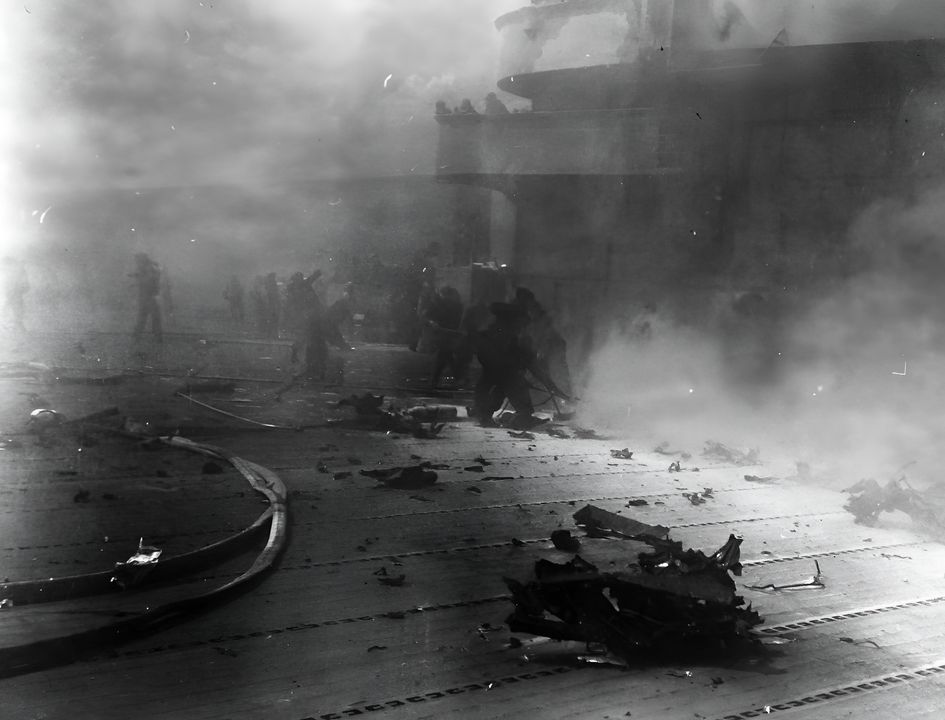 Các đội cứu hỏa cố gắng dập tắt ngọn lửa trên Hornet sau khi chiếc máy bay Type 99 đâm vào ống khói của đảo chỉ huy Hornet. Có thể thấy các mảnh vỡ máy bay rải rác ở xung quanh cùng với khói bụi mịt mù. (NHHC)